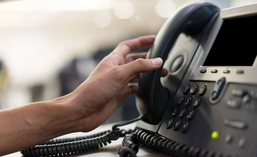 Hand picking up a desk IP phone in an office environment.