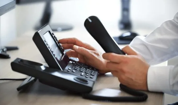 Person using a desktop IP phone handset to dial while seated at a workstation desk.
