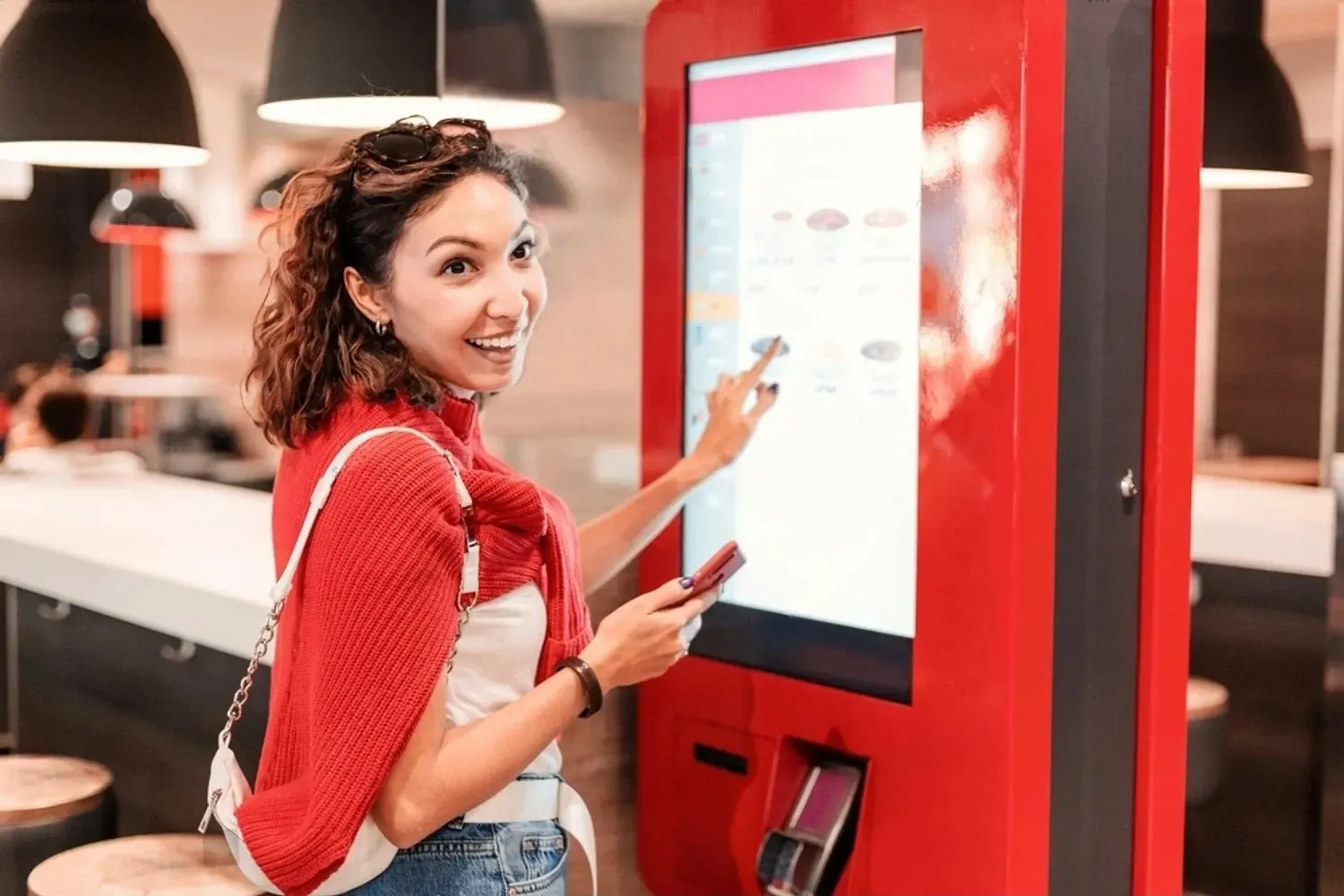 Smiling woman using a digital self-ticketing kiosk for queue management at a service point.