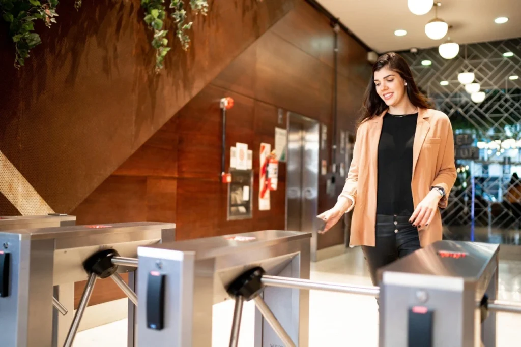Woman passing through tripod turnstile with card in hand, using secure mobile credential entry.
