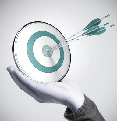 Hand holding target with arrows hitting bullseye.