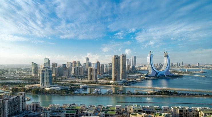 Aerial view of modern Qatar with crescent-shaped towers, skyscrapers, and turquoise waterfront.